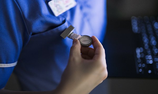 Nurse on duty at night, face unseen, checks the time on her fob watch. Many nurses on duty as the clocks go back are not paid for the extra hour