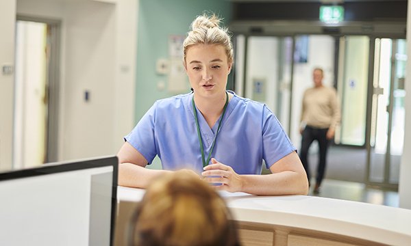 Agency nurse stigma: an agency nurse stands at a nurses' station on a ward talking to a permanent team member