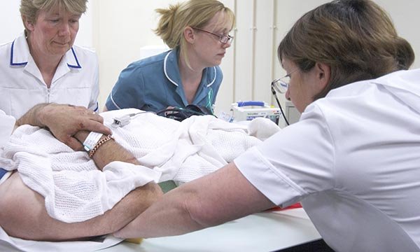 Women, who make up 90% of the nursing workforce, are at higher risk of back pain. A group of nurses use a slide sheet to move a patient.