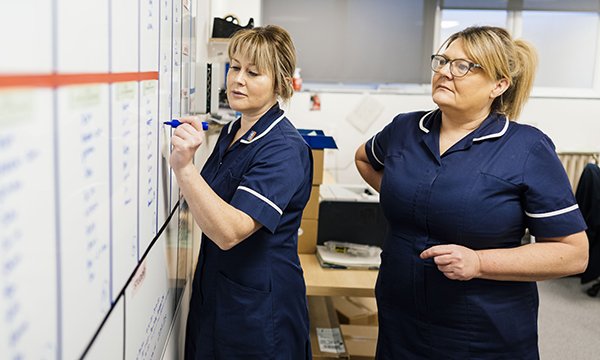 Senior nursing job profiles review: two nurses on shift updating a white board in a staff area