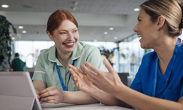 NMC revalidation for nurses: two nurse colleagues laugh together while having a discussion. A reflective discussion is required for revalidation