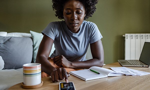 Financial hardship in nursing: a woman sitting at a table with her finger on a calculator key, working out personal living costs