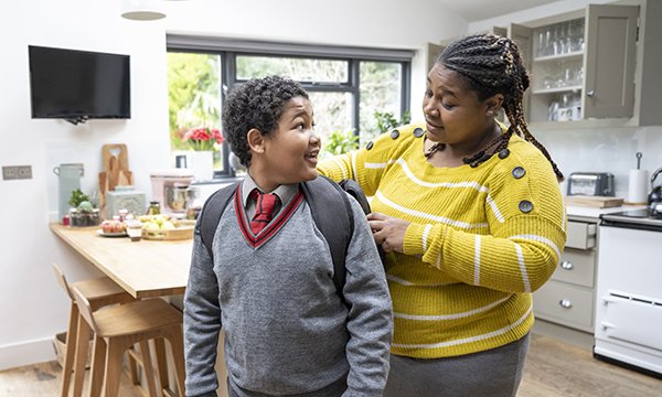 Juggling working and parenting as a nurse: a woman stands in a family kitchen as she helps her son get ready for school