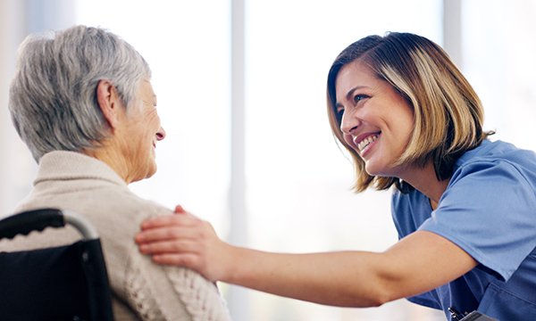 Compassionate dementia care: a smiling nurse places her hand on the shoulder of an older person, who is sitting in a wheelchair