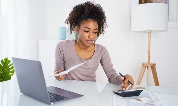 Nursing student loan forgiveness: young woman checks her finances using her laptop and calculator