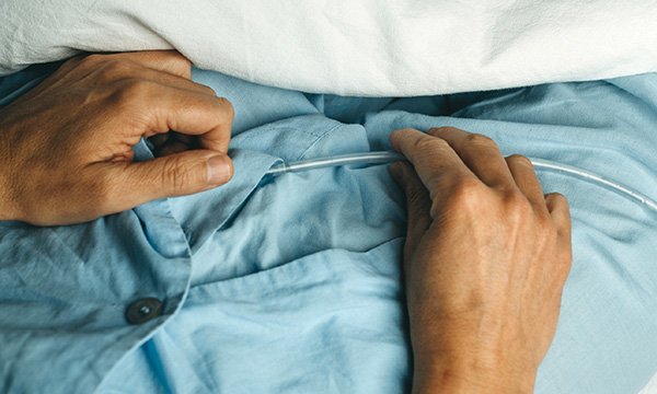 Catheter use and infections: close-up of a patient in pyjamas with their hands resting on top of a urinary catheter tube