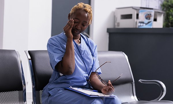 A nurse sitting in a workplace setting rubs her eyes as if feeling tired after a shift