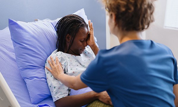 Trauma-informed nursing care: nurse comforts a weeping woman in a hospital bed