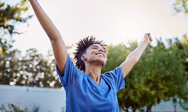Nurse career breaks: nurse stretches out her arms in happy relief, she is outdoors near trees