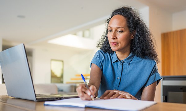 Nurse revalidation: woman works at home on laptop, making notes by hand