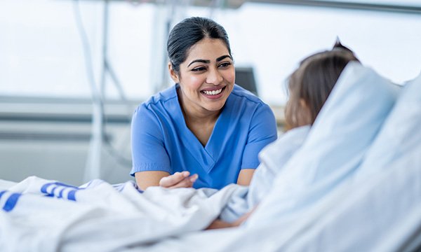 Pastoral care in nursing: nurse smiles broadly at bedside of a child in hospital 