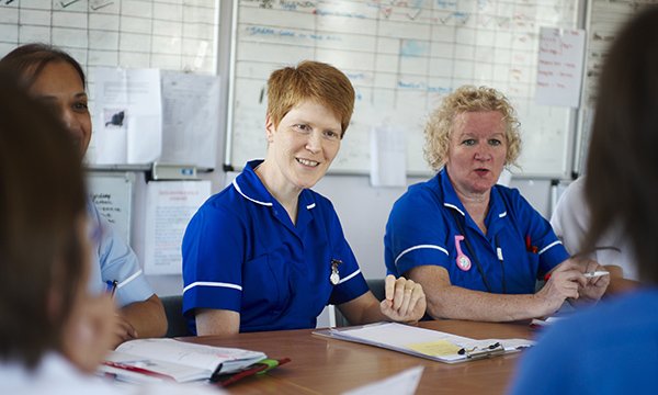 A group of nurses in discussion around a table. Nurses demonstrate their own approach to leadership each time they engage with nursing practice.