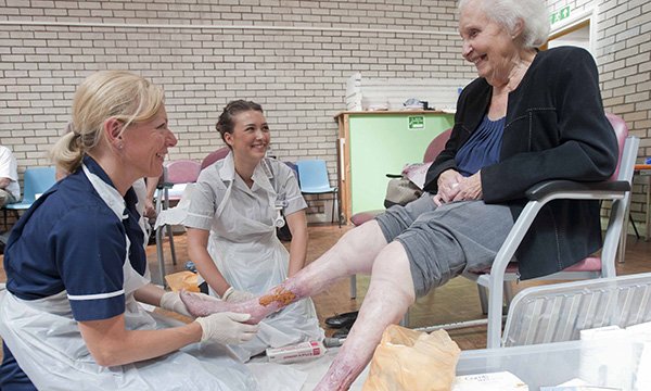 A tissue viability nurse examines a patient with leg wounds as a nursing student looks on