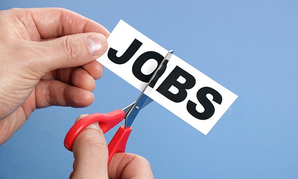 Cutting senior nursing roles: Image of a person using a pair of scissors as they cut across a label with the word JOBS in bold print on it