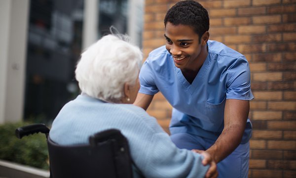 Social care placement: a nurse cares for a care home resident in a wheelchair as they converse in the outdoor area of the facility
