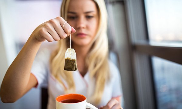 A woman holds a tea bag above a cup of tea