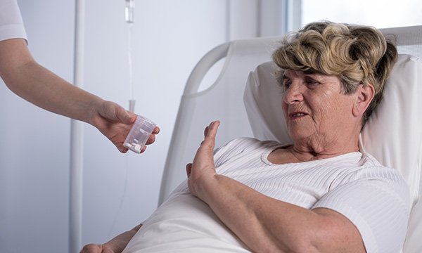 Patient in a hospital bed gestures to refuse her prescribed drugs