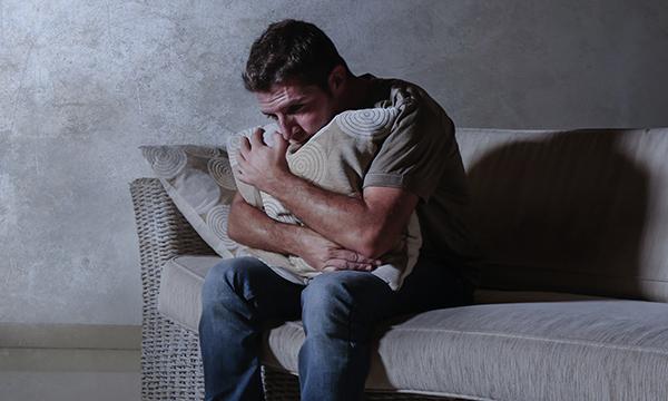 An isolated man hugs a pillow on a sofa. Mental healthcare and distress: Lack of nursing experience and confidence to manage distress can lead to a dependence on restraint, seclusion and/or enhanced observations