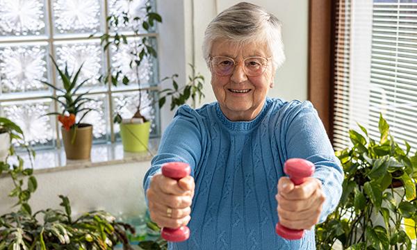 An older woman holding weights in each hand. Exercise should include weight-bearing and muscle-strengthening activities.