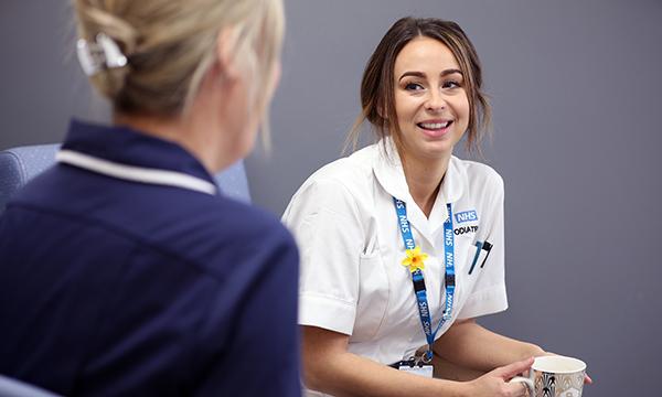 A young nurse smiling as she chats with a senior nurse during a break