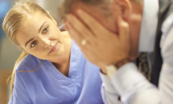 Young female nurse comforts middle aged man with head in his hands