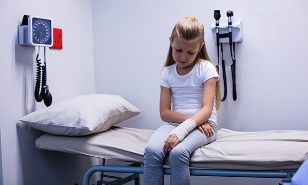 Young girl with bandaged arm sitting on hospital bed